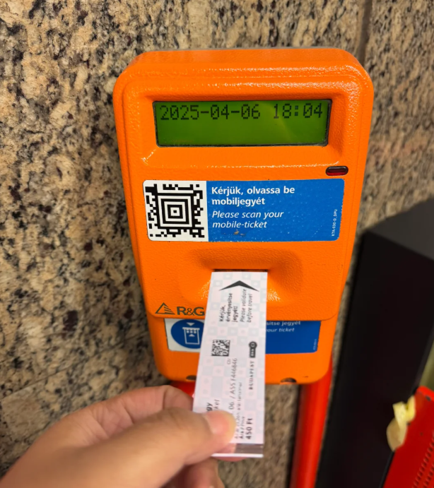 A tourist is using an orange ticket machine to validate their ticket