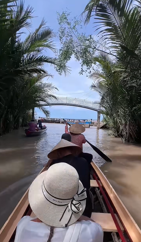 A woman in a conical hat paddling a traditional sampan boat through a lush Mekong Delta canal.