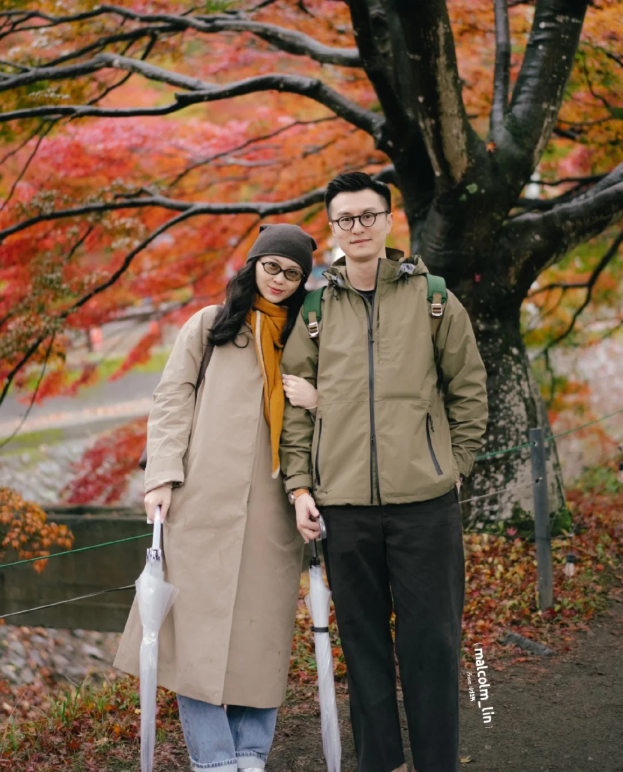 A couple wearing autumn clothes are admiring the red maple leaves